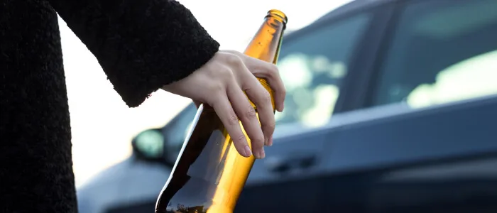 A man holds a beer bottle before getting into a car