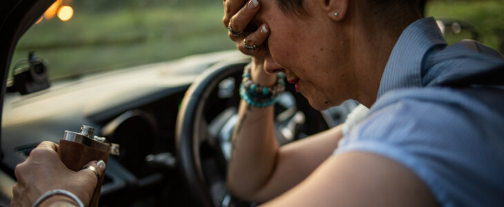 A mature woman sits behind the wheel and drinks brandy