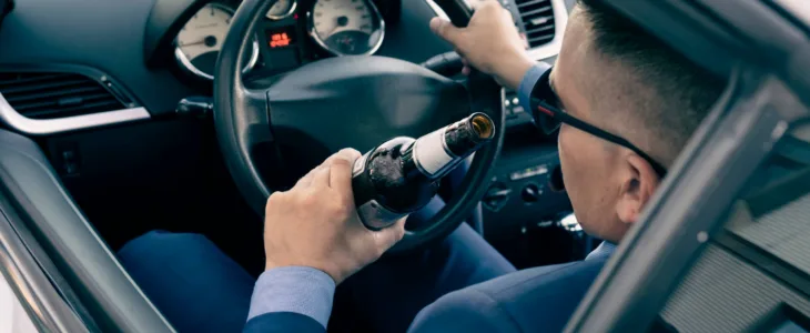 A man in an expensive suit drinks beer at the wheel of a car causing the danger of an emergency. A businessman drinks while driving. Drunk driver concept