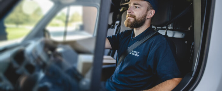 Side view of confident young independent delivery expert sitting in driver’s seat of van ready to begin transport.