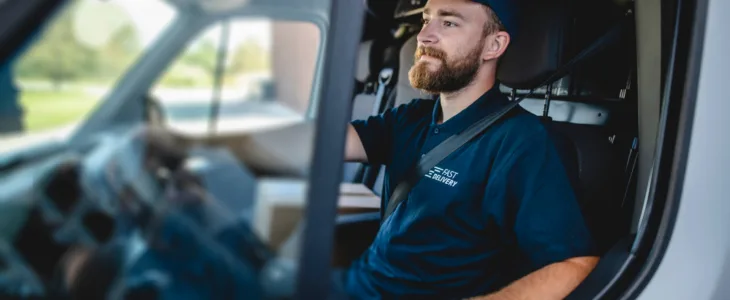 Side view of confident young independent delivery expert sitting in driver’s seat of van ready to begin transport.