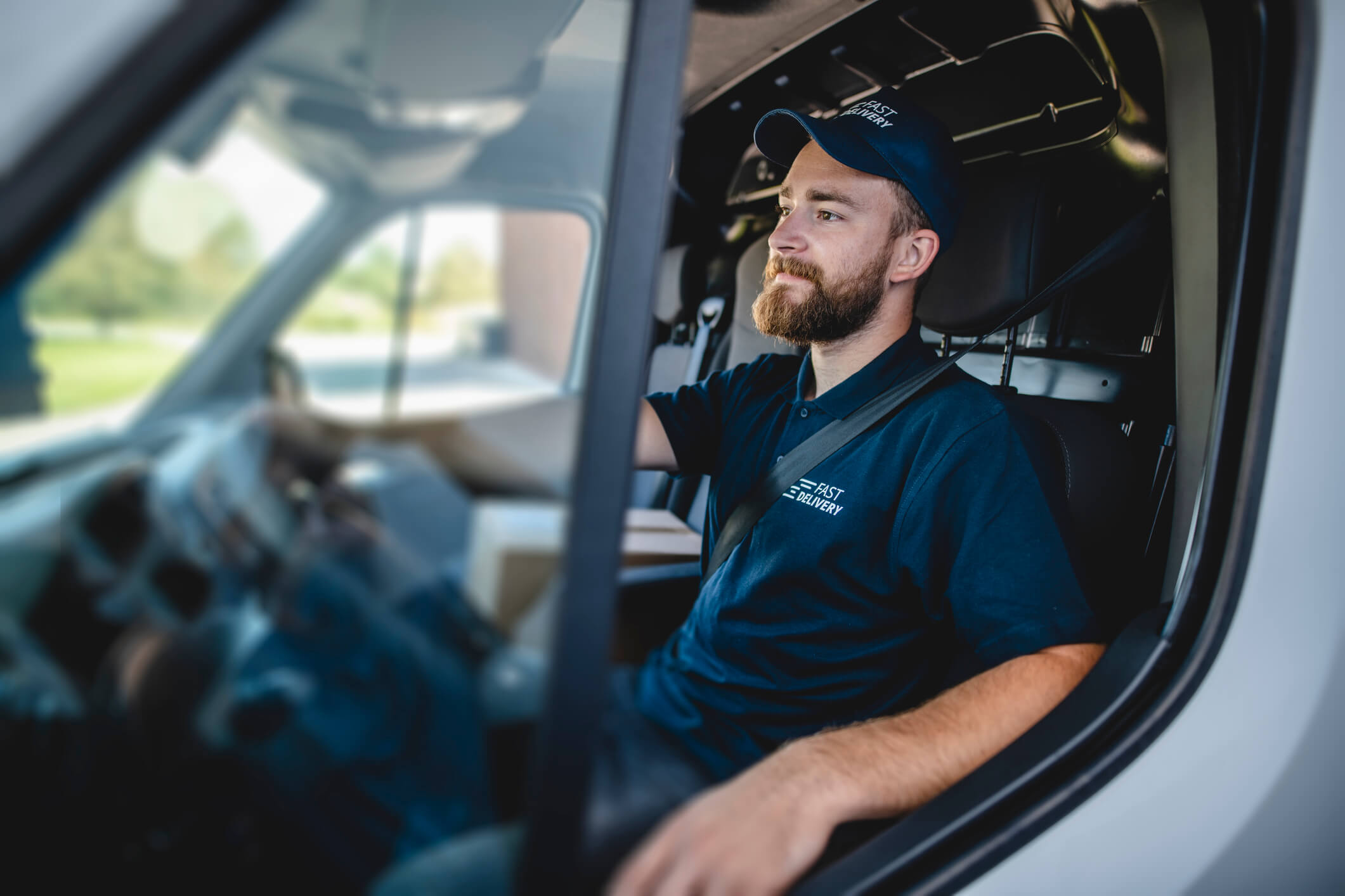 Side view of confident young independent delivery expert sitting in driver’s seat of van ready to begin transport.